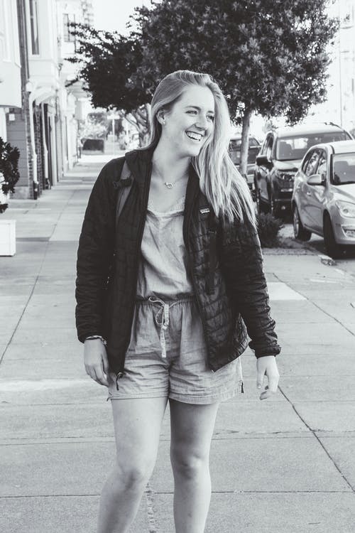 站立在路的微笑的妇女佩带的夹克的灰度照片 · 免费素材图片
