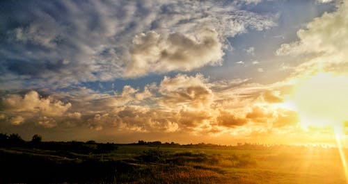 在日落的多云的天空下的绿草田 · 免费素材图片