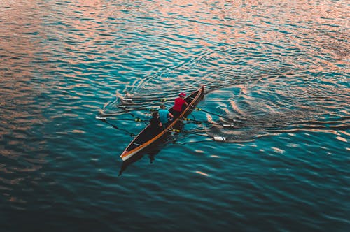 三人在平静的水面上航行的棕色独木舟 · 免费素材图片