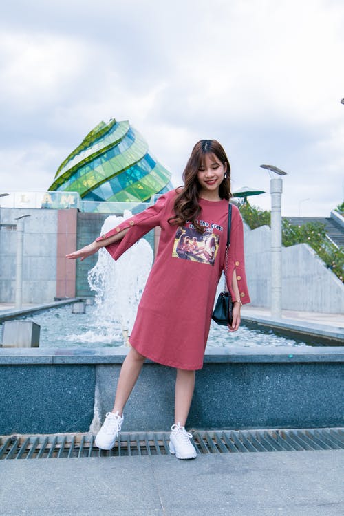 站在蓝色和白色的多云的天空下的灰色混凝土室外喷泉旁边的女人在白天 · 免费素材图片