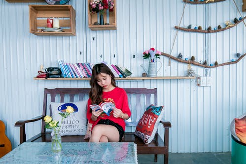 坐在长椅上的红衬衫阅读书中的女人 · 免费素材图片
