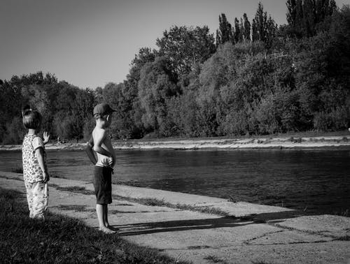 Oy男孩和女孩站在水体附近的灰度照片 · 免费素材图片