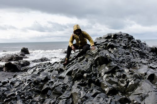在水体后面的石头上戴帽衫的男人的选择性彩色摄影 · 免费素材图片