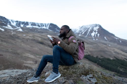 男人穿着棕色夹克和蓝色的裤子，坐在绿色的草地，拿着矩形的情况下 · 免费素材图片