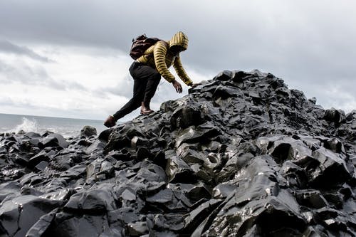 男人穿着连帽衫和黑色裤子爬上一堆岩石 · 免费素材图片