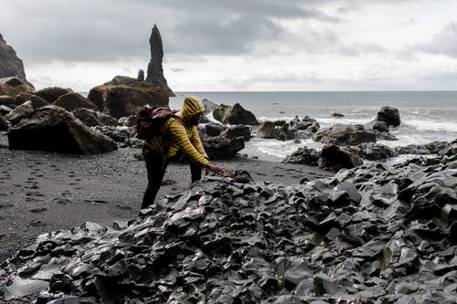 在海边穿连帽衫摸石头的人 · 免费素材图片