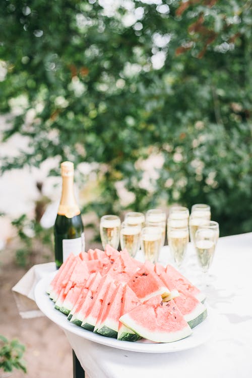 一束切成薄片的西瓜在香槟瓶附近的白碗中的选择性聚焦照片 · 免费素材图片