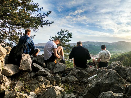四名男子坐在面对山的岩石上 · 免费素材图片