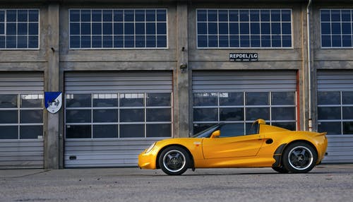 黄色小轿车停在棕色油漆仓库附近 · 免费素材图片
