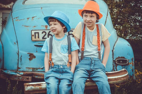 两个男孩坐在经典蓝色汽车的后保险杠上 · 免费素材图片
