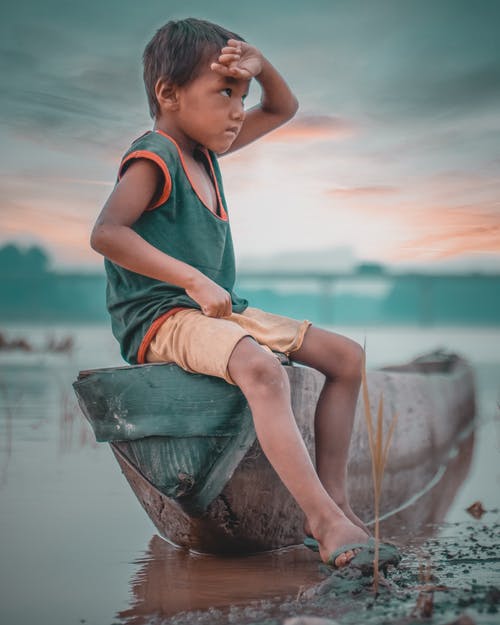 男孩坐在独木舟附近白云下采取的水体 · 免费素材图片