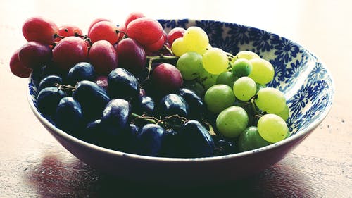 圆形蓝色和白色花卉陶瓷碗中的红色，黑色和绿色葡萄 · 免费素材图片