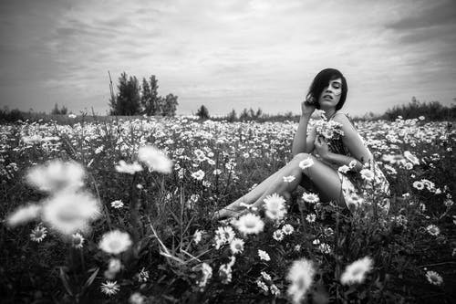 女人坐在雏菊旁边的灰度照片 · 免费素材图片
