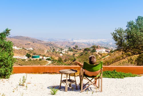 白天坐在树和山在蓝蓝的天空下附近的绿色椅子上的人 · 免费素材图片