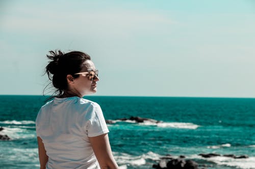 女人穿着白色t恤在海上与岩层的距离 · 免费素材图片