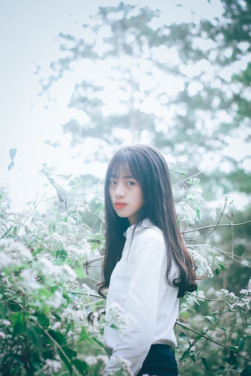 女人穿着白色纽扣的长袖衣领的衬衫站在白色花瓣花旁边 · 免费素材图片