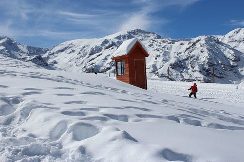 穿着红色外套的人在雪中的棕色房子附近的照片 · 免费素材图片