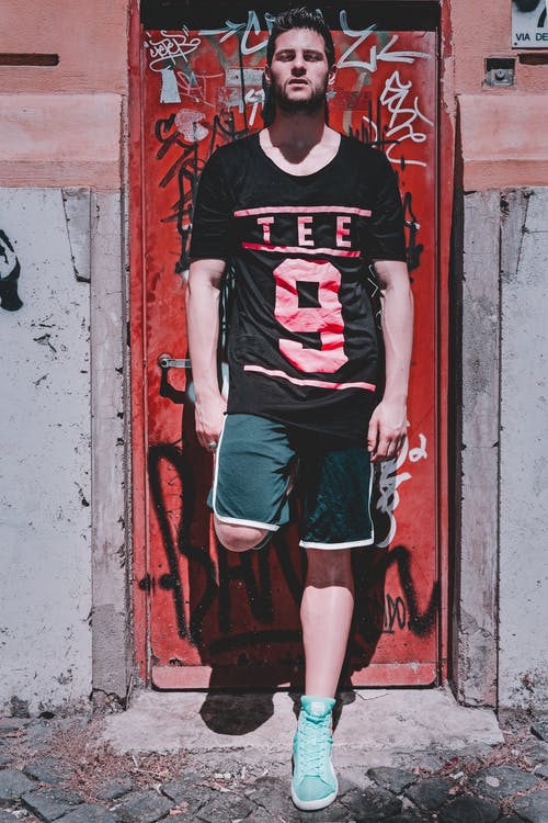 男子倚在红色金属门上的照片 · 免费素材图片