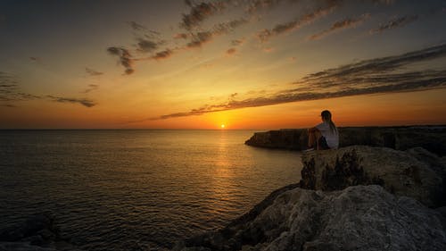 在日落期间坐在岩石上的人的照片 · 免费素材图片