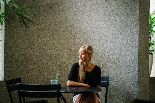 坐在黑色金属椅子上的黑色瓢顶上衣的女人 · 免费素材图片