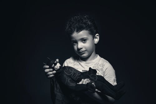 一个男孩抱着蝙蝠侠毛绒玩具的灰度照片 · 免费素材图片