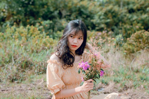 女人穿着米色露肩礼服捧着鲜花的浅焦点摄影 · 免费素材图片