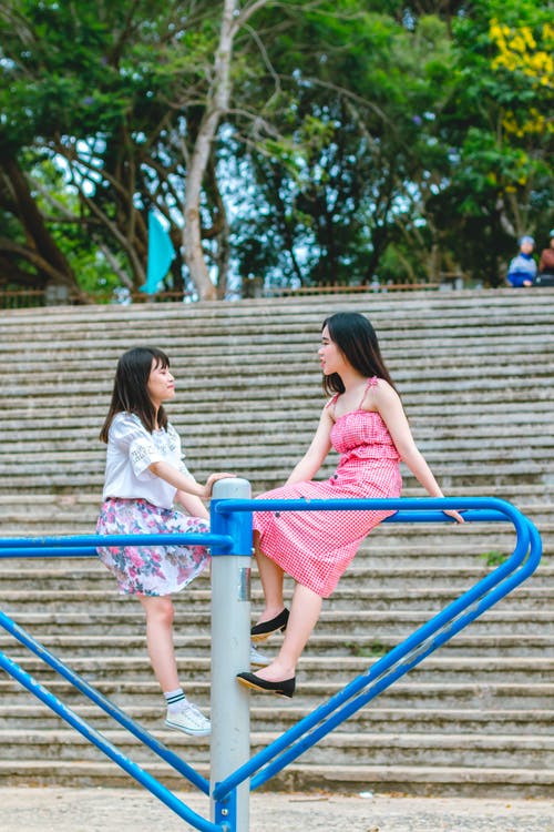两个女孩坐在蓝色的金属机架上 · 免费素材图片
