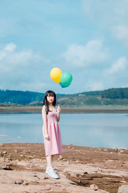 女人拿着气球站在米色的沙滩上 · 免费素材图片
