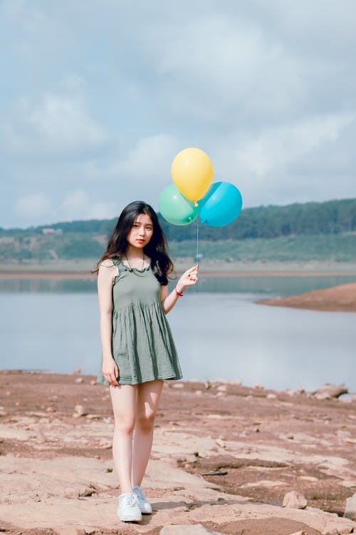 女人的穿着绿色无袖连衣裙拿着3个气球 · 免费素材图片