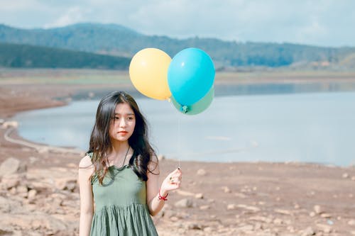女人拿着三个各色气球的浅焦点摄影 · 免费素材图片
