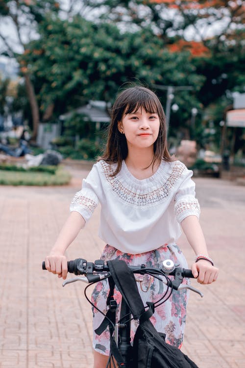女人穿着白色的衬衫和多彩多姿的花裙子骑自行车 · 免费素材图片