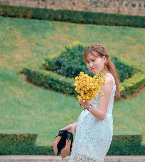 女人穿着白色蕾丝连衣裙，拿着黄色的花花束 · 免费素材图片