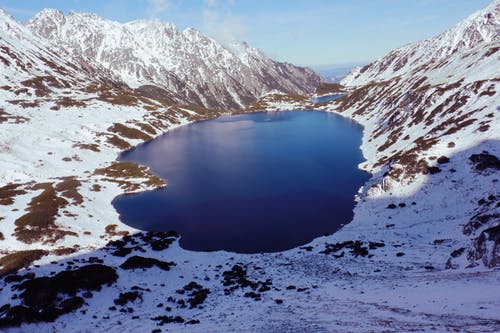大雪覆盖的山脉之间水体的高角度视图 · 免费素材图片