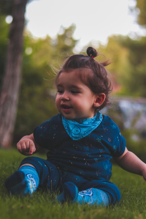 婴儿穿蓝色连身衣和袜子坐在绿草上的照片 · 免费素材图片