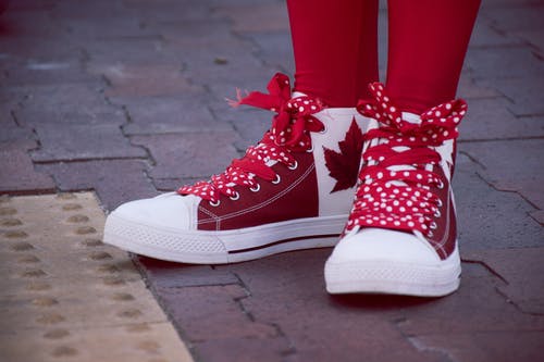 身穿白色和红色枫叶印花花边运动鞋的人的特写照片 · 免费素材图片