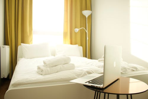 Macbook空气在床附近的棕色木制的桌子上 · 免费素材图片