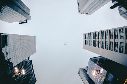 高层建筑上空飞行的飞机的低角度摄影 · 免费素材图片