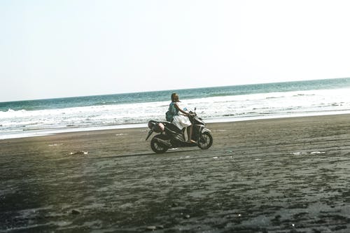 女人在海滩上骑黑色和灰色的小型摩托车 · 免费素材图片