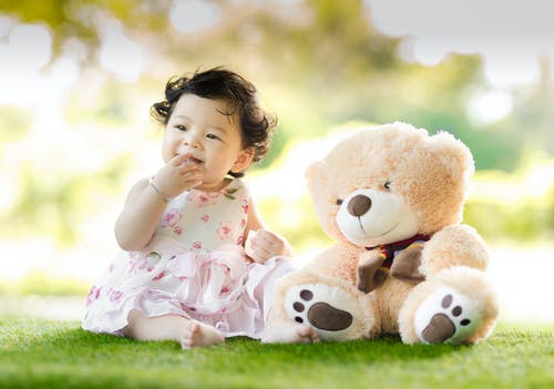 婴儿在白天坐在熊毛绒玩具旁边的绿草 · 免费素材图片