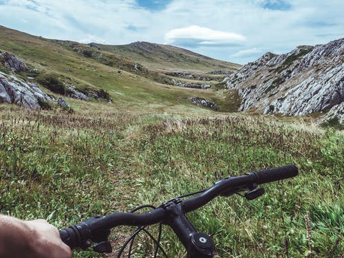 人骑自行车俯瞰绿草田和山 · 免费素材图片