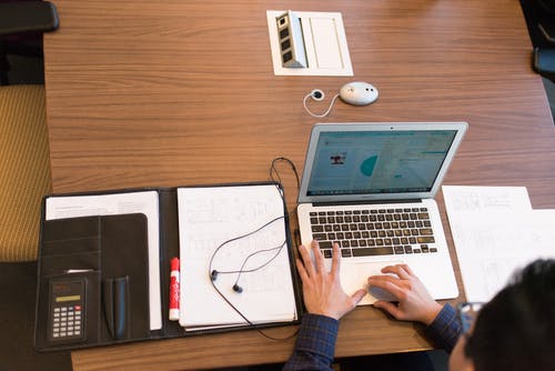面对棕色木制的桌子上的白色笔记本电脑的蓝色礼服衬衫的人 · 免费素材图片