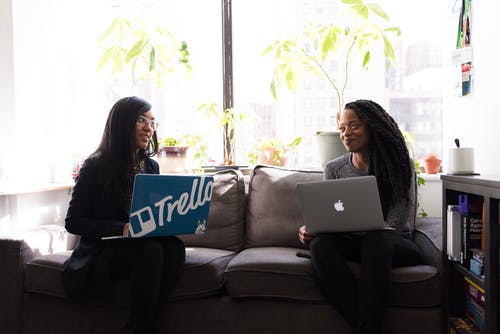 两名妇女坐在灰色织物2座沙发上，手提电脑时互相凝视 · 免费素材图片