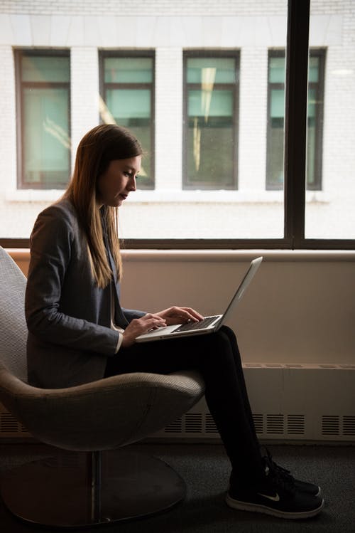女人坐着，靠近窗户使用便携式计算机 · 免费素材图片
