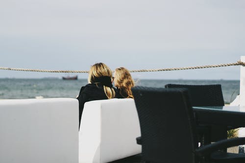 两个女人坐在水边附近 · 免费素材图片