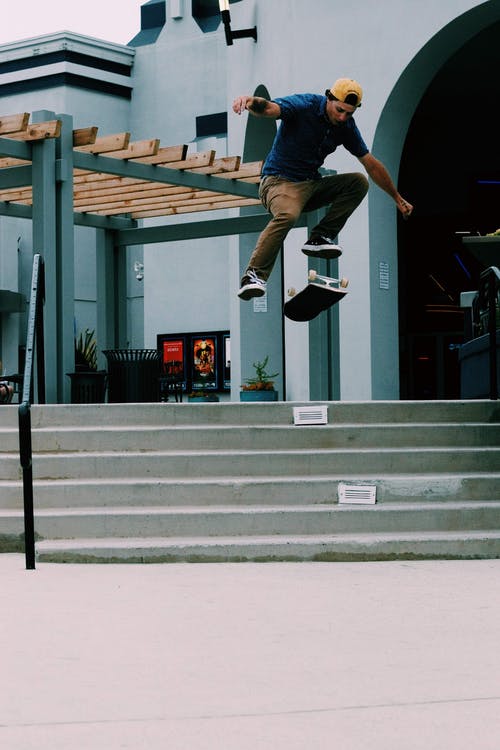 男子跳过翻转滑板的空气 · 免费素材图片