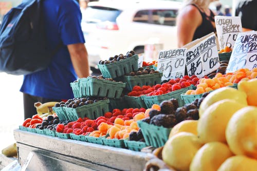身穿蓝色上衣和黑色下衣的人站在水果摊附近 · 免费素材图片