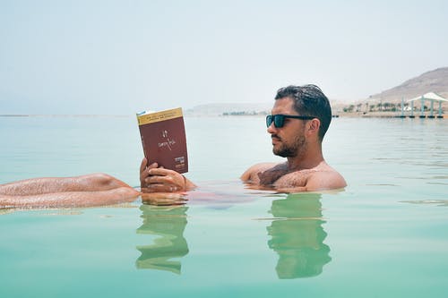 戴墨镜的男子在水体上读书 · 免费素材图片