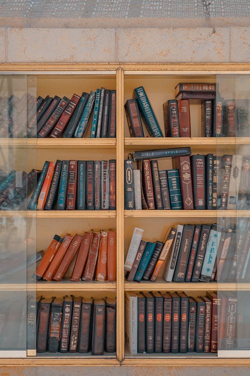 棕色木框玻璃壁挂柜内的书籍分类标题 · 免费素材图片