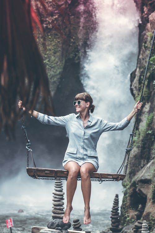 女人坐在秋千椅上与瀑布背景 · 免费素材图片