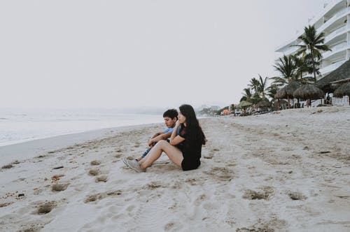 男人和女人坐在沙滩上 · 免费素材图片